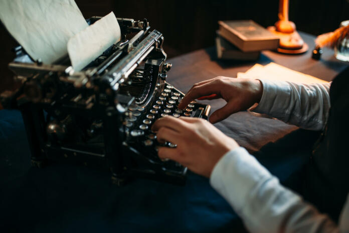 Portrait of bearded literature author in glasses typing on vintage typewriter. Creative people concept