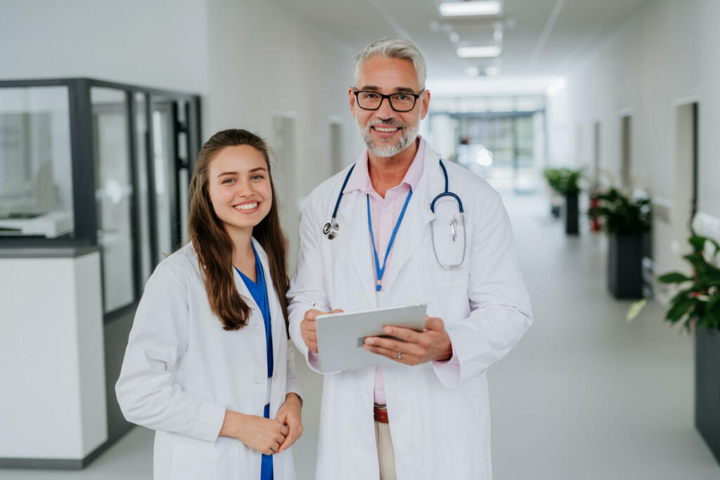 Portrait of elderly doctor with his younger colleague at a hospital corridor. Health care concept.