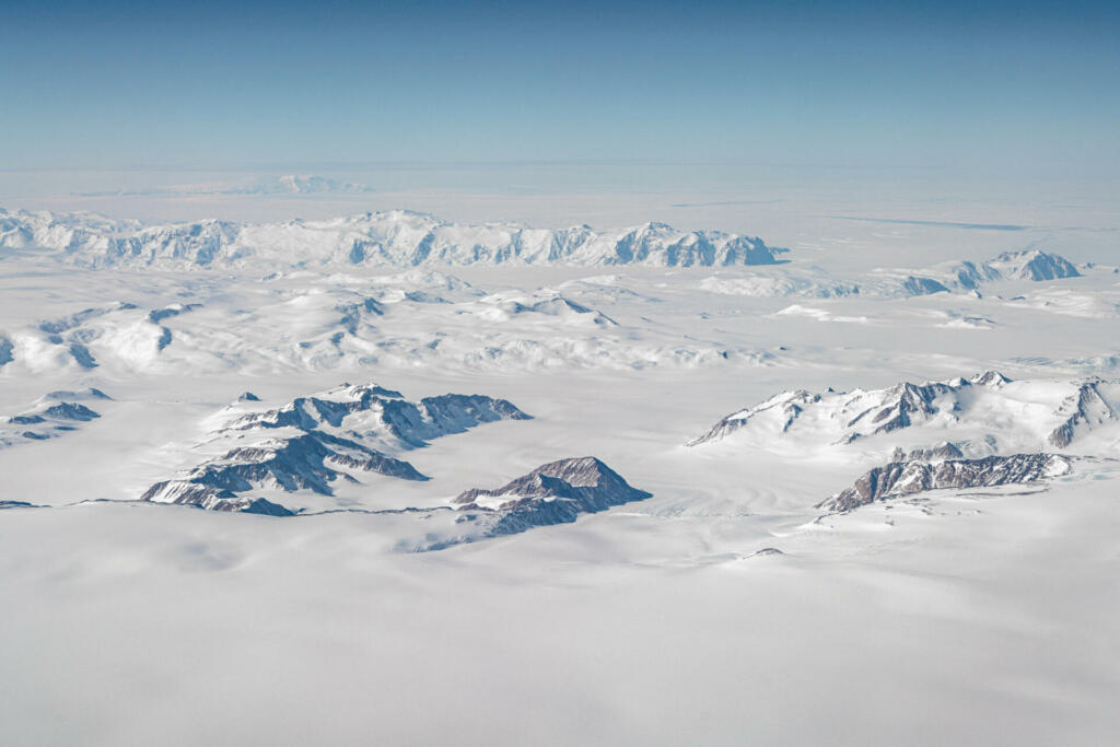 Seen from the sky ice cap on the antarctic continent with emerging mountain peaks