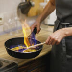 Woman preparing caramelized banana flambe with cognac in frying pan and sets fire