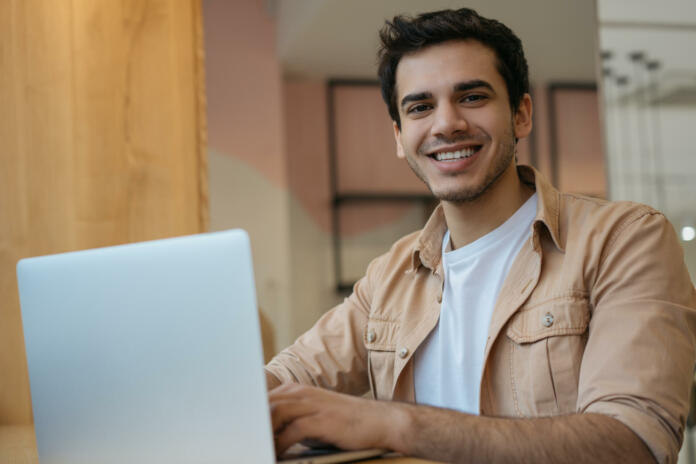 Young asian student studying, e-learning , online education concept. Portrait of handsome Indian businessman using laptop computer, working at home. Copywriter typing on keyboard, looking at camera