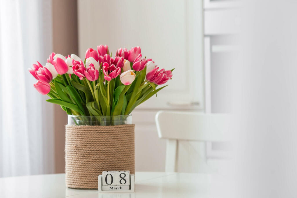 A bouquet of tulips on a white table. In the background, the interior of a white kitchen in the Scandinavian style. The concept of home comfort.The concept of International Women's Day on March 8.