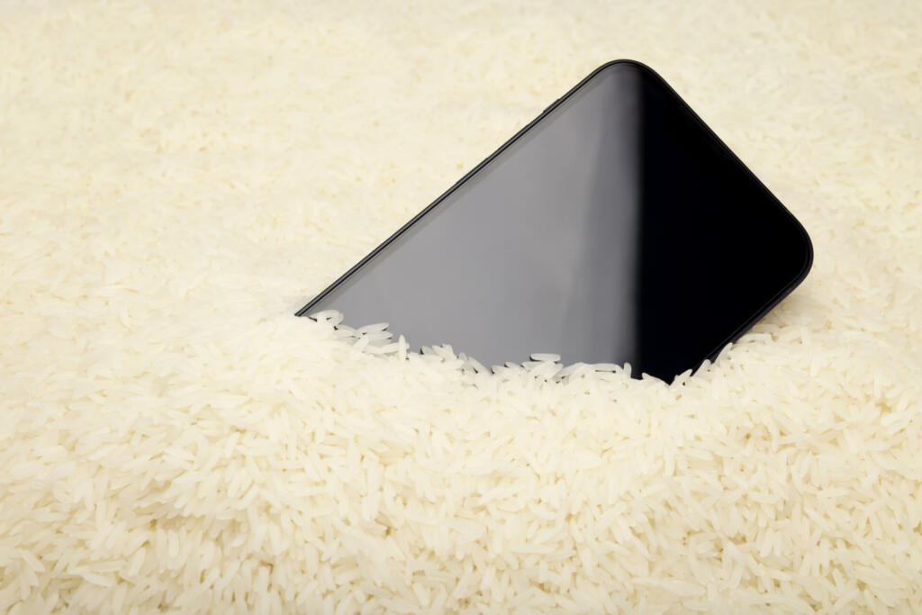A wet smartphone is dried in raw rice on white background