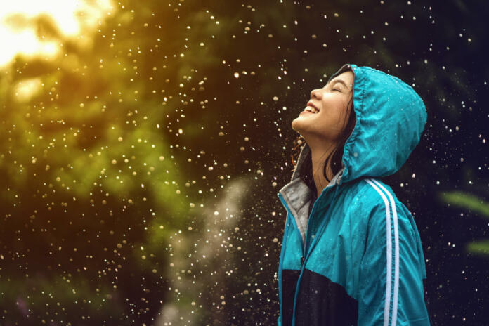 Asian woman wearing a raincoat outdoors. She is happy.