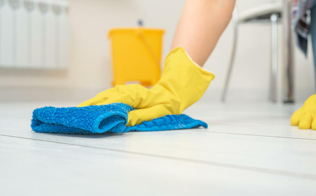 Cleaning service. crop image of woman thoroughly and gently washing and cleaning white laminate floor. female hands in yellow gloves wipe wooden floor with blue microfiber cloth. copy space