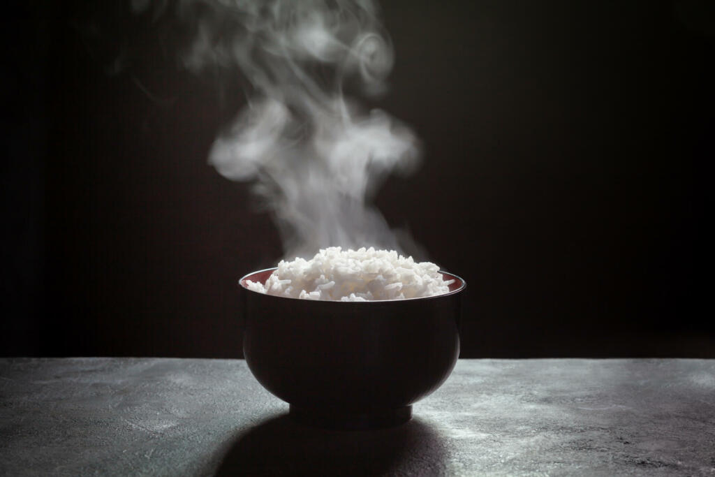 Cooked rice with steam in black bowl on dark background,hot cooked rice in bowl selective focus,hot food and healthy