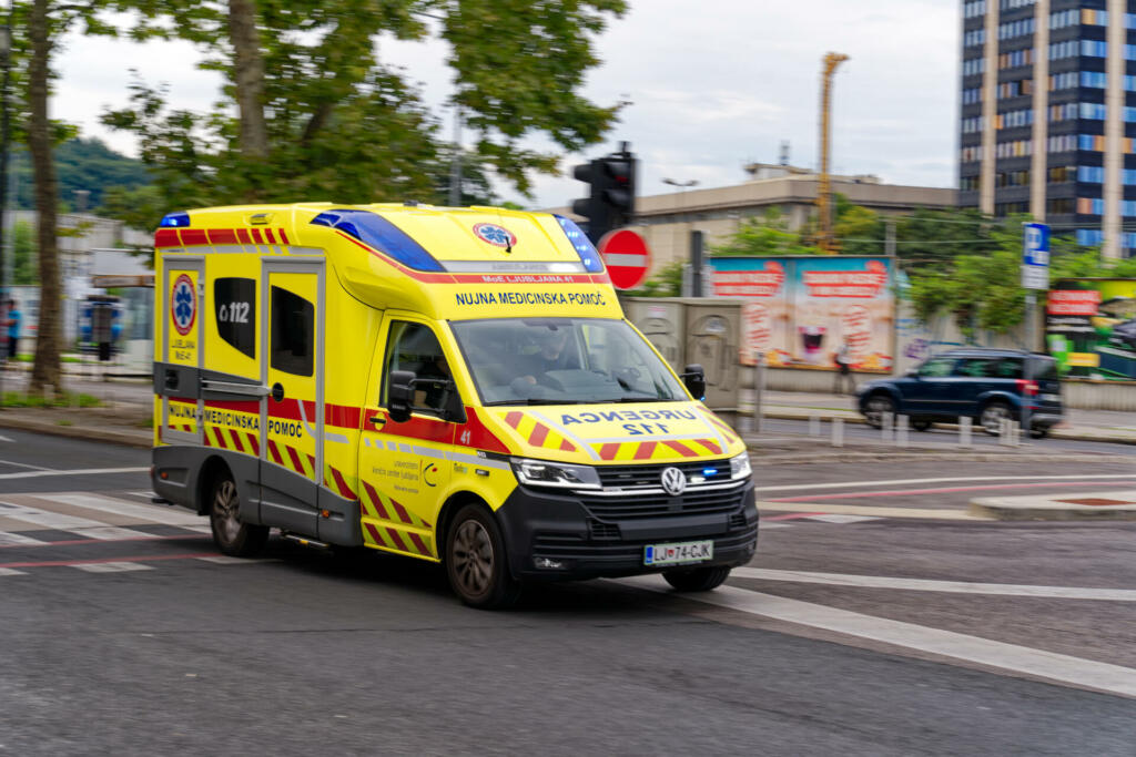 Fast driving blurry yellow green ambulance van with blue lights and siren at City of Ljubljana on a cloudy summer day. Photo taken August 9th, 2023, Ljubljana, Slovenia.