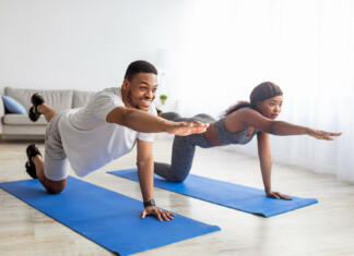 10 vaj za moč in stabilizacijo trupa brez opreme Fit black couple stretching their arms and legs, doing yoga or pilates on mat indoors. Motivated African American family working out at home during covid quarantine. Stay home hobbies