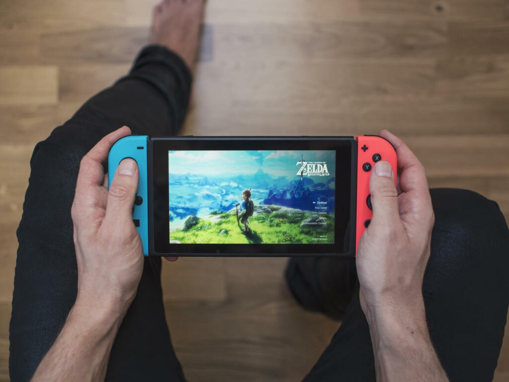 Gothenburg, Sweden - March 10, 2017: A shot from above of a young man's hands holding a neon coloured Nintendo Switch video game system developed and released by Nintendo Co., Ltd. in 2017. The system is turned on and the game The Legend of Zelda, Breath of the Wild is showing on the display. Shot on a hardwood floor background in a home environment.