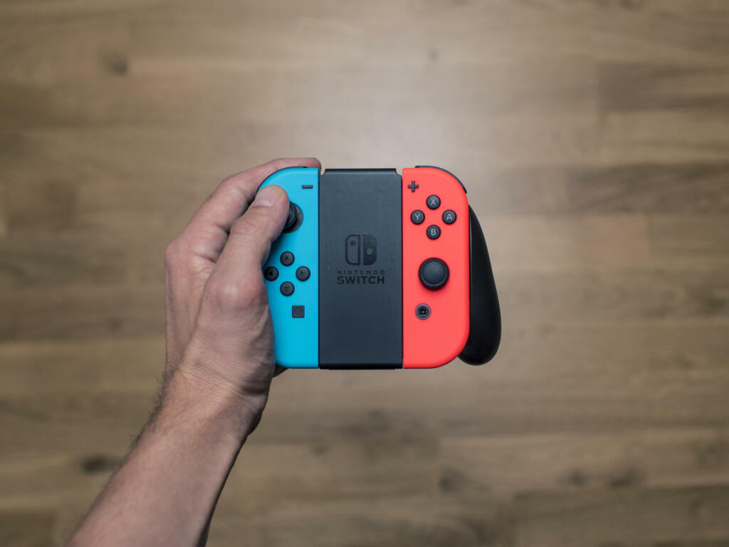 Gothenburg, Sweden - March 6, 2017: A shot from above of a young man's hand holding a Nintendo Switch game controller, a neon coloured remote controller for the Nintendo Switch video game system developed and released by Nintendo Co., Ltd. in 2017. Shot on a wooden background in a home environment.