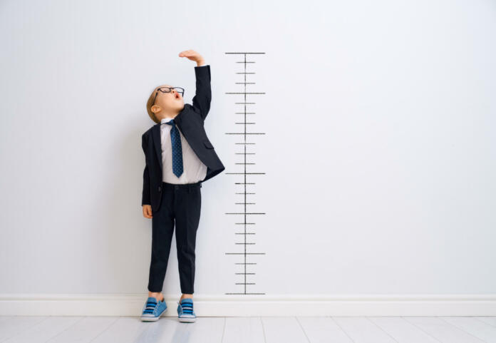Little child is playing businessman. Kid is measuring the growth on the background of wall. Smart power concept.