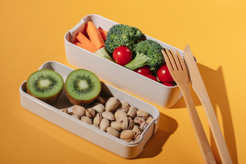 Lunch box with fresh vegetables, fruits and nuts on yellow background