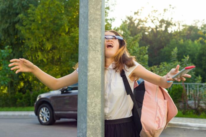 Portrait of young inattentive girl, distracted by mobile phone. Girl crashed into street post, dropped phone