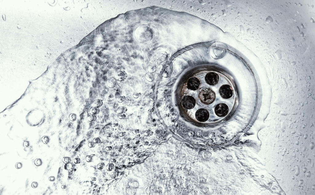 water drain down on stainless steel kitchen sink hole. top view sewer in washbasin. household plumbing. cleaning and hygiene concept.