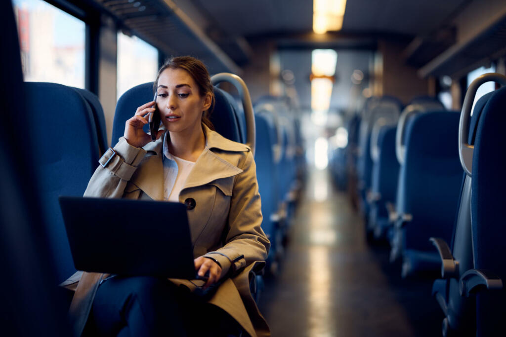 Young businesswoman talking on cell phone while using laptop in a train.
