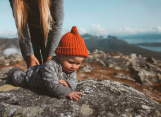 Kako v hribe z dojenčkom in najmlajšimi? Baby learning crawling outdoor family vacation mother with child infant wearing orange hat autumn season in Norway
