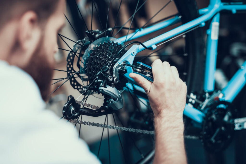 Bike Mechanic Repairs Bicycle in Workshop. Closeup Portrait of Young Blurred Man Examines and Fixes Modern Cycle Transmission System. Bike Maintenance and Sport Shop Concept