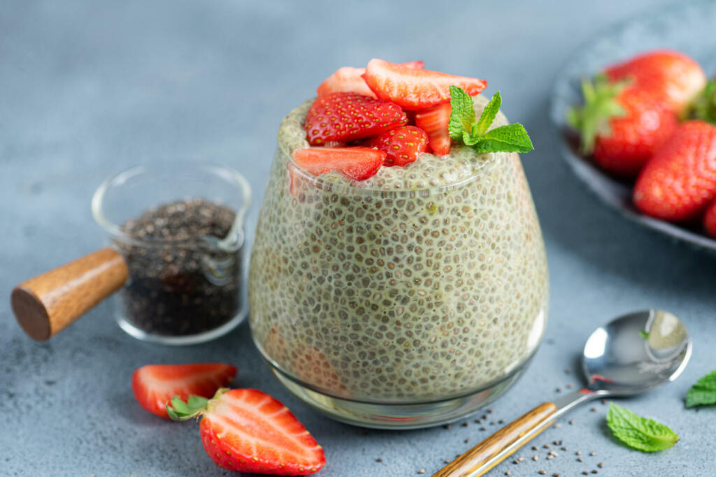 Chia pudding with strawberries in glass jar on blue stone background, closeup view