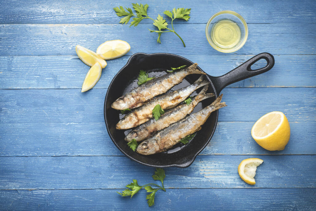 Fried sardines on the small  а frying pan in a marine style served with  parsley, lemons and olive oil. Blue wooden background, marine style, top view, copy space
