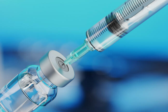 Medical disposable syringe for vaccine injection and glass vial on blue blur background.