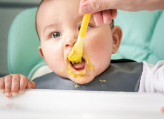 Srhljiva afera velikega podjetja: Kar počne je nemoralno, pravijo Mom feeds the baby with a spoon of vegetable puree at the children's feeding table. Baby's appetite, healthy nutrition, introduction of complementary foods. Copyspace, mock up