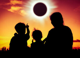 Kdaj bomo pri nas videli popolni sončni mrk? Natural phenomenon. Silhouette back view of family sitting and relaxing together. Boy point to solar eclipse on gold sky background. Happy family spending time together. Outdoor.