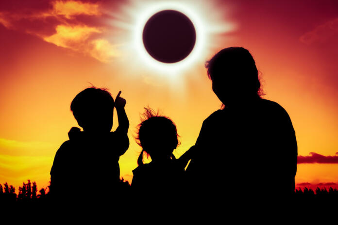 Natural phenomenon. Silhouette back view of family sitting and relaxing together. Boy point to solar eclipse on gold sky background. Happy family spending time together. Outdoor.