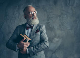 Pisatelji z najboljšim stilom, a ne tistim, na katerega bi najprej pomislili Portrait with copy space of successful, attractive, serious millionaire in jacket, glasses, holding three books in arms, with serious expression looking to the side over gray background