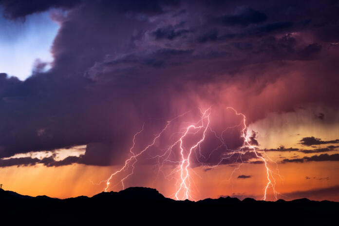 Powerful lightning bolts strike from a sunset thunderstorm in the Arizona desert.