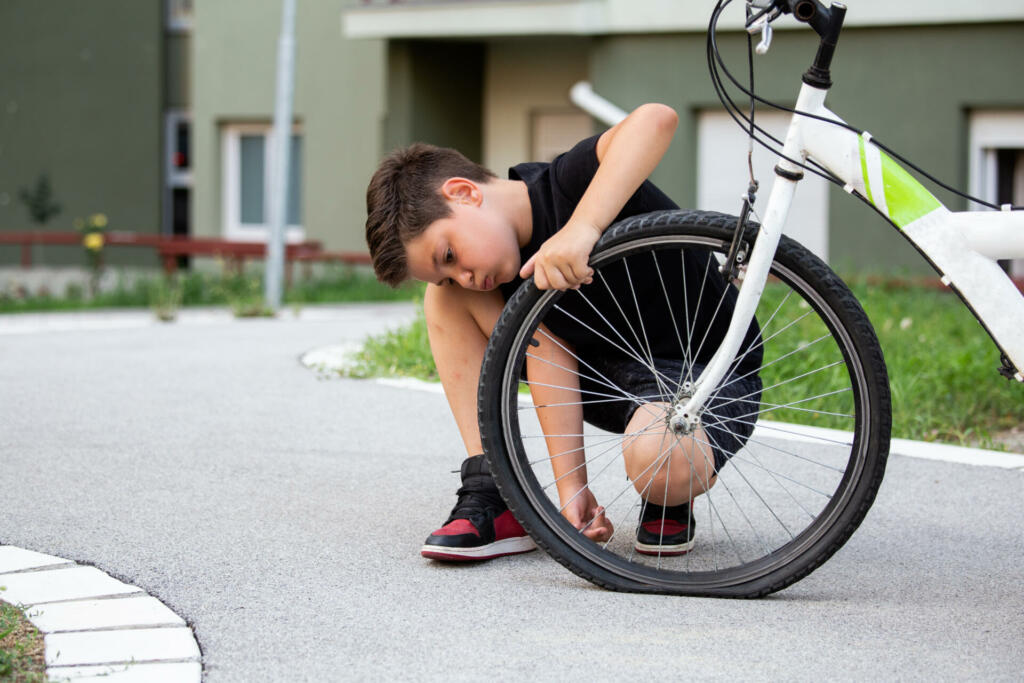 Sad boy looking at his flat bike tire, kid staring at the bicycle with the broken wheel