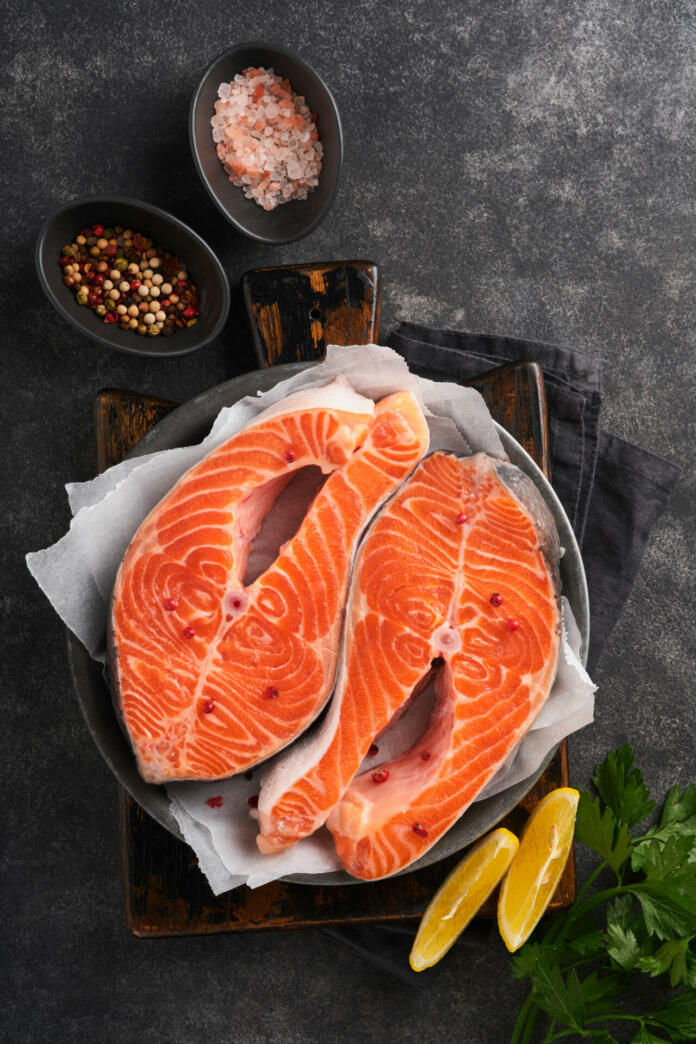 Salmon. Raw salmon steak. Fresh raw salmon fish with cooking ingredients, herbs and lemon prepared for grilled baking on black background. Healthy food. Top view. Copy space.