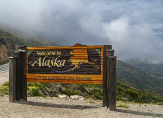 Top 10 Aljaska: Destinacije, ki jih moraš obiskati Skagway, Alaska, USA - July 20, 2011: Klondike highway to Canada. Colorful Welcome sign near the border. Cloudscape in back.
