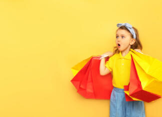 Z malčkom po nakupih? Otročje lahko! Surprised child girl in summer clothes hold package bag with purchases isolated on yellow background studio. Shopping discount sale concept. Mock up,copy space, banner. Black friday