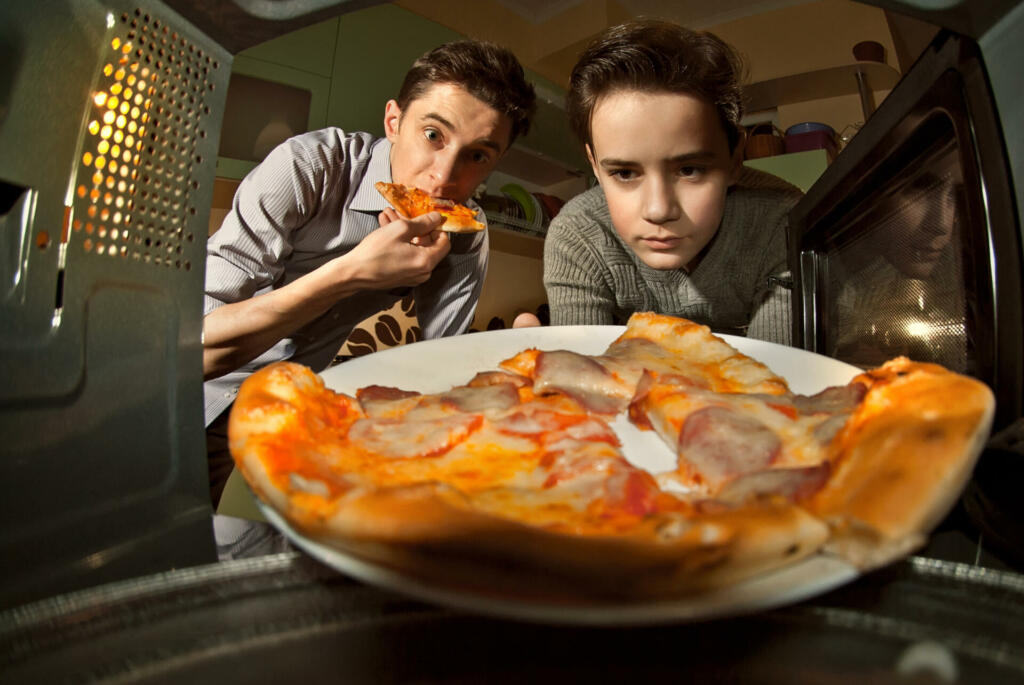 The guys get pizza from the microwave. Food heating in the home kitchen. Fast food. Cooking at home. Men eating pizza.