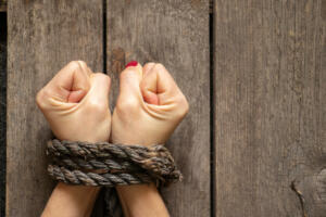 tied female hands with rope on wooden background close up