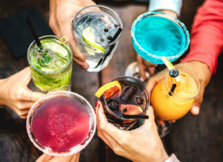 Kako pripraviti koktajl po trendih leta 2024? Top view of people hands toasting multicolored fancy drinks - Young friends having fun drinking cocktails at happy hour - Social gathering party concept on vivid filter - Shallow depth of field