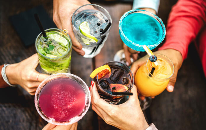 Top view of people hands toasting multicolored fancy drinks - Young friends having fun drinking cocktails at happy hour - Social gathering party concept on vivid filter - Shallow depth of field