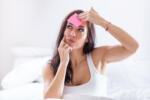 Woman forgetting something puts a pink post-it on her forehead, thinking.