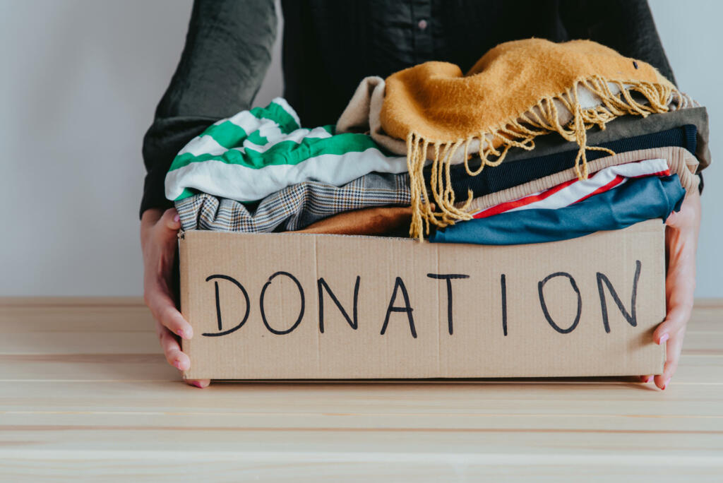 Woman holding cardboard donation box full with clothes. Concept of volunteering work, donation and clothes recycling. Helping poor people