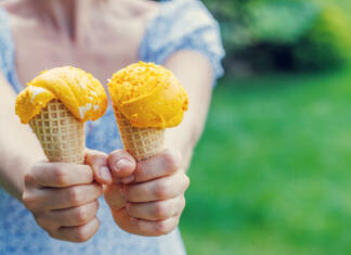 Sladoled, sorbet ali gelato: kakšne so razlike? Woman's hands holding refreshing ice cream in waffle cones treats with a hint of zesty lemon flavour. With copy space