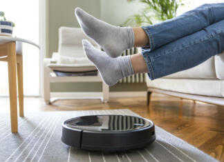 Ali so robotski sesalniki res nezanesljivi? Young woman lift up the feet for letting robotic vacuum cleaner pass though