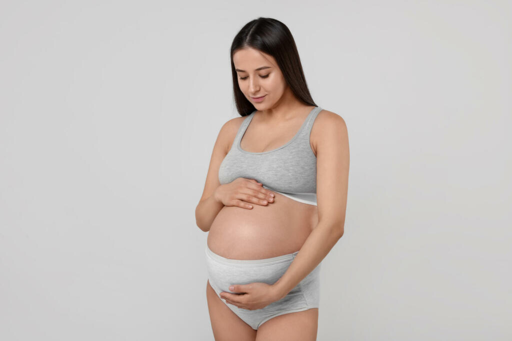 Beautiful pregnant woman in comfortable maternity underwear on grey background