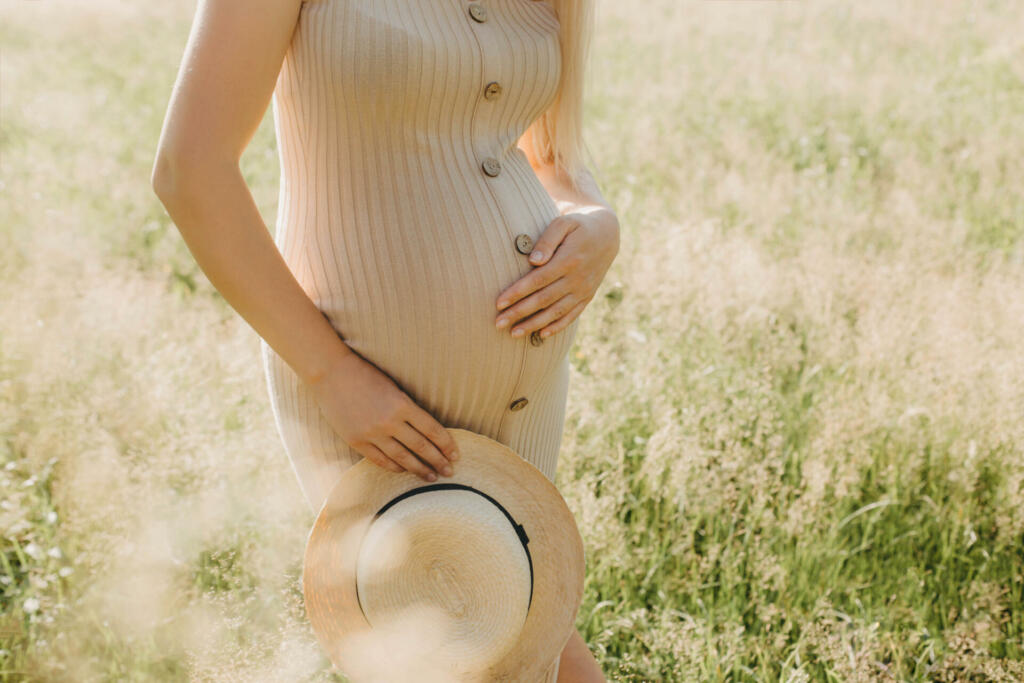 Beautuful hipster blonde pregnancy woman in a hat and tight dress in the summer park. Trendy young parents, outdoor portrait.