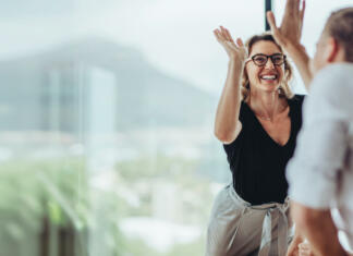 Novartis BioCamp 2024: Prijave so že odprte Businesswoman giving a high five to male colleague in meeting. Business professionals high five during a meeting in boardroom.