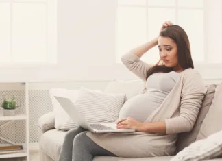 Zanimive spremembe v nosečnosti (si že slišala zanje?) Confused pregnant woman using laptop, sitting on sofa at home. Young expectant lady surfing net, remote working, buying goods for newborn. Online shopping, pregnancy concept, copy space