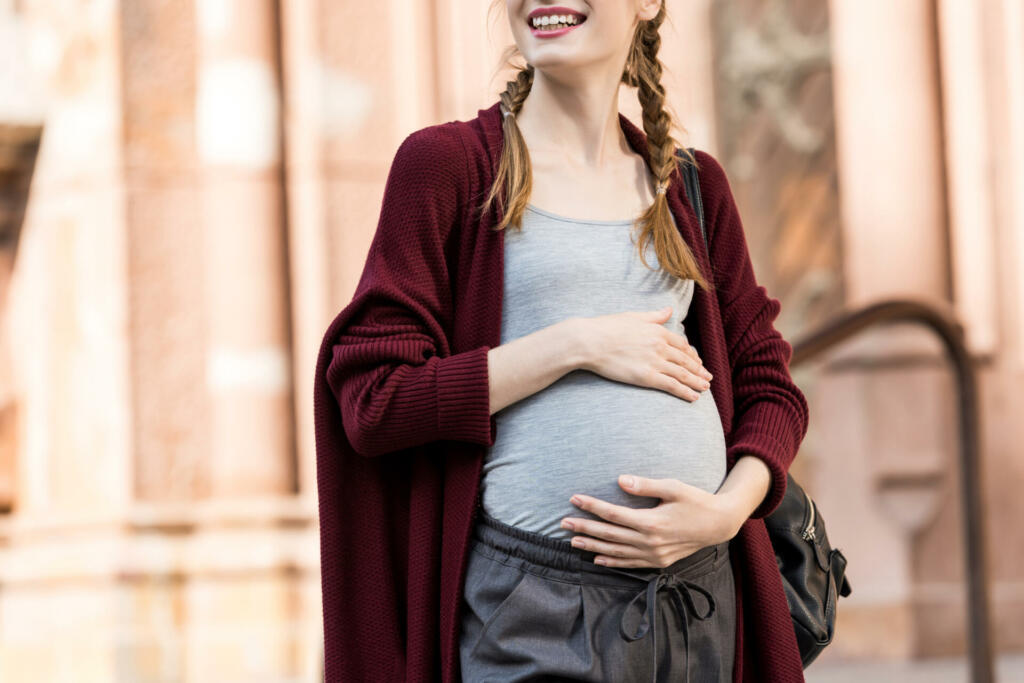 cropped shot of happy pregnant woman touching belly and looking away on street