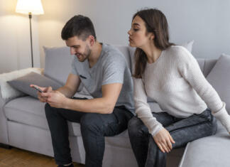 Način, kako preprečiti radovedne poglede na svoje osebne podatke Emotional upset couple sitting on couch and quarreling about smartphone, mistrust concept. Jealous suspicious mad wife arguing with obsessed husband holding phone texting cheating on cellphone