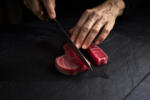 Female cook preparing a piece of bluefin tuna to make sushi on a blackboard. Asian food concept