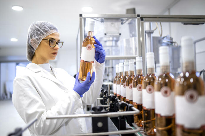 Female factory expert controlling wine production in alcohol beverage bottling plant.