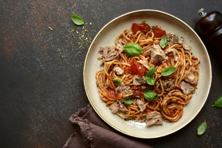 Italian pasta spaghetti with tuna in tomato sauce on a dark slate, stone or concrete background. Top view with copy space.